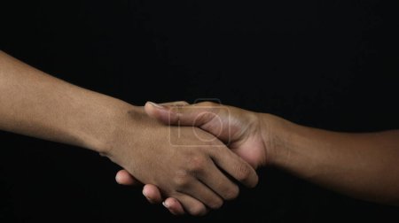 Cerca de dos hombres estrechando la mano como acuerdo sobre fondo negro.