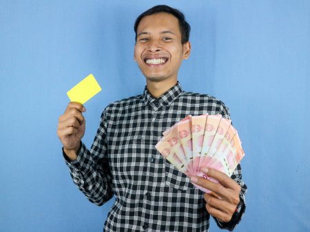 Excited expression handsome asian man hold empty card and money banknotes. Business and finance concept.