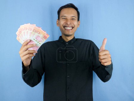 Foto de Emocionado expresión guapo asiático hombre celebrar billetes de papel moneda con golpes hasta gesto. Concepto de negocio y finanzas. - Imagen libre de derechos