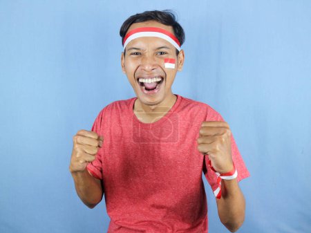 Excited expression young indonesian man wearing red and white headband with clenching fist gesture. Independence concept, 17 August