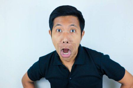 funny expression of shocked and surprised Asian man wearing a black t-shirt looking at the camera