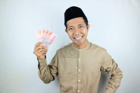 Glücklicher Gesichtsausdruck eines asiatischen muslimischen Mannes, der auf weißem Hintergrund isolierte Rupiah-Banknoten hält