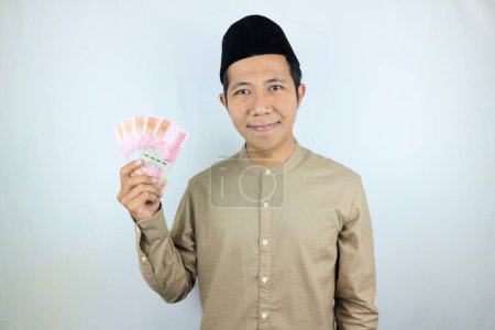 Feliz expresión del hombre musulmán asiático sosteniendo billetes de rupias de dinero aislados sobre fondo blanco
