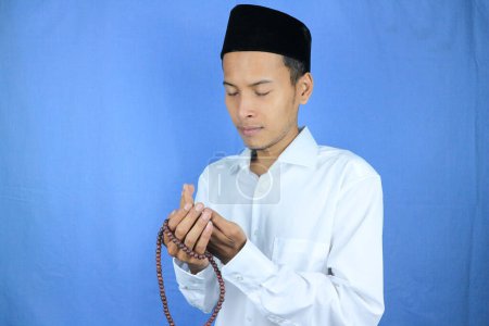 Hombre asiático musulmán sosteniendo cuentas de oración sobre fondo azul. Ramadán kareem y ied concepto mubarak.