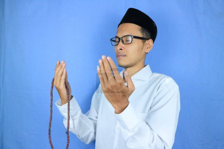 Muslim asian man holding prayer beads on blue background. Ramadan kareem and ied mubarak concept.