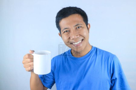Lächelnder Ausdruck junger asiatischer Mann im T-Shirt mit Kaffeetasse, isoliert auf weißem Hintergrund
