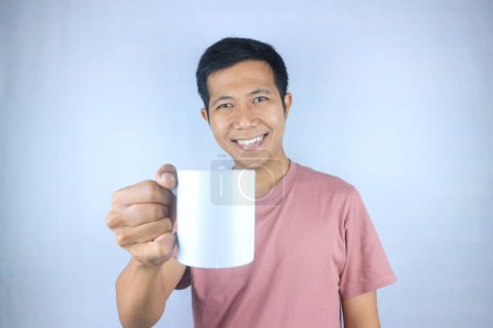 Lächelnder Ausdruck junger asiatischer Mann im T-Shirt mit Kaffeetasse, isoliert auf weißem Hintergrund