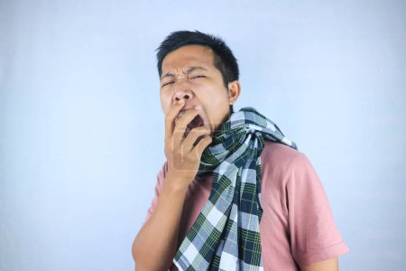 Tired young indonesian man wearing a sarong and yawning, feeling sleepy. Bedtime concept