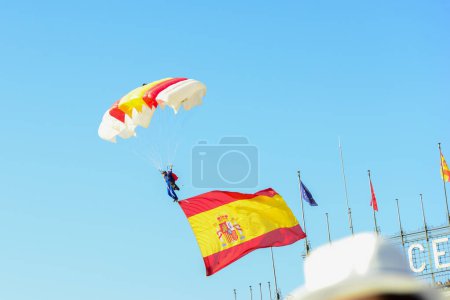 Téléchargez les photos : Caporal Maria Carmen Gomez atterrit avec un parachute et le drapeau de l'Espagne. Quelque 4 100 militaires ont participé au défilé militaire de la fête nationale, dont le roi Felipe VI, la reine Letizia et la princesse Leonor, à Madrid, en Espagne.. - en image libre de droit