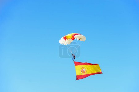 Téléchargez les photos : Caporal Maria Carmen Gomez atterrit avec un parachute et le drapeau de l'Espagne. Quelque 4 100 militaires ont participé au défilé militaire de la fête nationale, dont le roi Felipe VI, la reine Letizia et la princesse Leonor, à Madrid, en Espagne.. - en image libre de droit