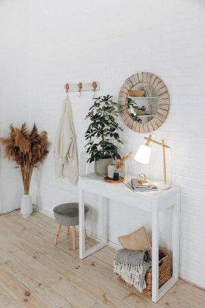 Photo for Console table with a potted plant, a table lamp and a round mirror in a wooden frame in a modern stylish living room in a Scandinavian style. Nobody. - Royalty Free Image