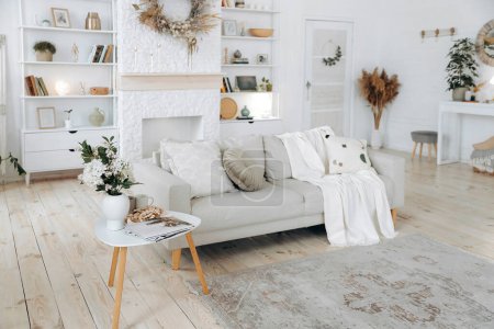 Photo for Scandinavian style sofa with plaid and pillows and coffee table in modern stylish bright living room with fireplace, shelving and console table. Nobody. - Royalty Free Image