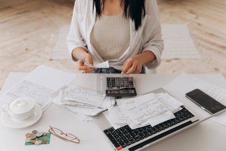 Top view of a woman working at home with financial papers on white office desk, paying bills, counting on a calculator, planning a budget to save some money. Independent accounting, remote accountant.