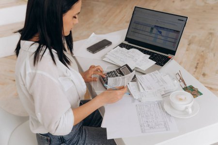 Photo for Side view of confident woman calculates utility expenses on laptop and calculator, engaged in online bill payments and financial documentation, concept of financial advice and remote work platforms. - Royalty Free Image