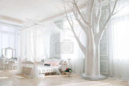 Ätherisches Schlafzimmer mit weißem Himmelbett, Pastellkissen, verzierten Eitelkeiten, großem weißen Baumdekor, Blumenstrauß, Sonnenlicht, das durch schiere Vorhänge strömt, luftiges und ruhiges Ambiente.