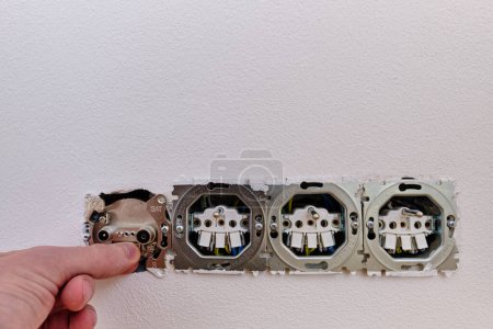 Photo for Electrician installing and adjusting electric outlet socket on a white wall and a Tv SAT plug. Uncovered boxes, contacts, metal frame, paint. - Royalty Free Image