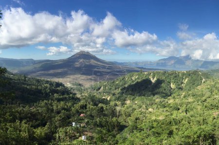 Vista panorámica del volcán Monte Batur rodeado de exuberante vegetación y montañas distantes en Bali, Indonesia. La imagen captura una escena natural serena y majestuosa.