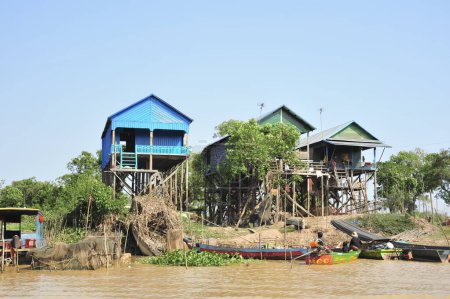 A group of houses are built on stilts over a body of water in Siem Reap Angkor Wat Cambodia. The houses are blue and green