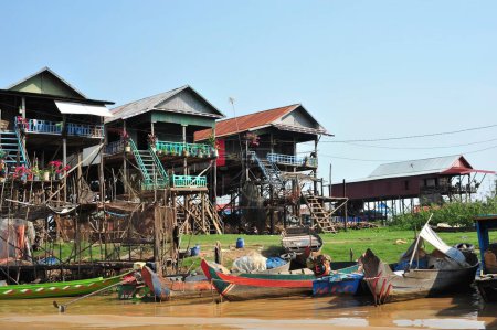 Vibrant image of traditional stilt houses on the riverbank in Cambodia with colorful wooden boats moored, depicting local life and culture.