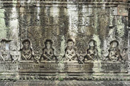 El muro está cubierto de estatuas de personas sentadas en Siem Reap Angkor Wat Camboya. La pared es vieja y tiene mucho musgo creciendo en ella.