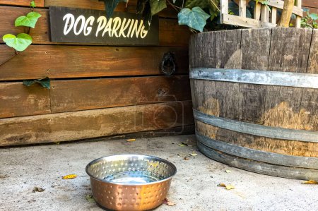 A quaint scene featuring a 'Dog Parking' sign above a water bowl, situated beside a rustic wooden barrel, conveying a warm, pet-friendly environment.