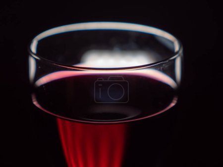 Artistic close-up of an illuminated red wine glass on a black background