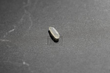 Foto de Un primer plano de una píldora de arroz sobre una superficie oscura con un fondo borroso - Imagen libre de derechos