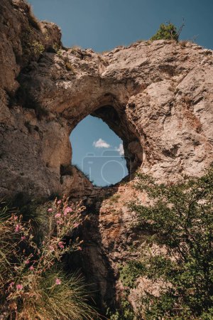 Téléchargez les photos : Hole in old rock with trees, grass, flowers and blue sky view. Natural attraction of Balkans. Dupni kamen is tourist landmark of Stara planina mountain range. Serbian natural site in Balkan Mountains. - en image libre de droit