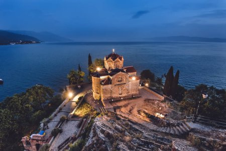 Photo for Church of Saint John the Theologian by Ohrid lake at night. St John at Kaneo church on cliff overlooking Lake Ohrid, night view with lights. Popular landmark of Ohrid town, Balkans travel destination. - Royalty Free Image