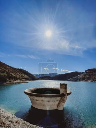 Photo for Dam spillway funnel rises up above lake surface, view from the bank. Water discharge funnel at the dam of Rovni lake, popular natural attraction. Travel Balkans, exploring Serbian natural landmarks. - Royalty Free Image
