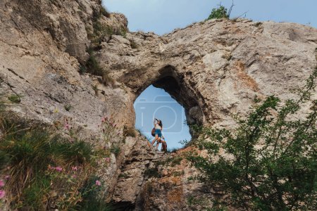 Photo for Young woman with vizsla dog standing in hole in rock against blue sky. Female on pet-friendly vacation exploring natural attractions. Backpacker girl traveling in Balkan mountains with pointer dog. - Royalty Free Image