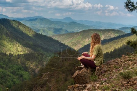 Téléchargez les photos : Femme randonneuse assise seule sur un rocher de montagne. Fille voyageur surplombe la vallée avec les jambes croisées, assis sur le bord de la falaise et regardant loin. Femme grimpé au sommet jouissant paysage de montagne à partir de pic. - en image libre de droit