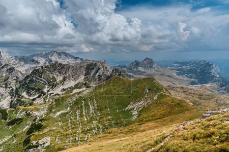 Foto de Paisaje de verano de montaña con un cielo dramático sobre las montañas de los Alpes Dináricos en el Parque Nacional Durmitor, Montenegro. Paisaje alpino con verde valle de montaña y senderismo en la cresta de la montaña. - Imagen libre de derechos