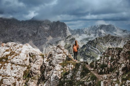 Photo for Woman hiker standing with her back on rock overlooking mountain landscape with dramatic clouds over Dinaric Alps in Durmitor National Park. Solo female traveler on rock in highlands with great view. - Royalty Free Image