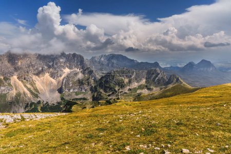 Foto de Paisaje montañoso de verano en las tierras altas del Parque Nacional Durmitor, Alpes Dináricos, Montenegro. Luz dorada iluminando cadenas montañosas e idílico valle verde bajo cielo azul con nubes blancas. - Imagen libre de derechos