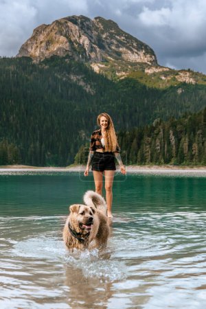 Téléchargez les photos : Jeune femme heureuse jouant avec le chien de berger Kangal dans le lac de montagne pendant les vacances d'été acceptant les animaux de compagnie. Femme active s'amusant avec son animal de compagnie dans le lac noir dans le parc national de Durmitor, Monténégro. - en image libre de droit