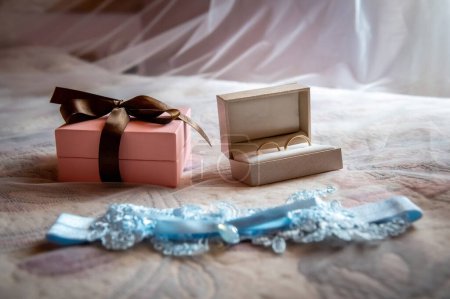 Foto de Guardarropa de novia y novio y prendas de vestir liga nupcial azul acostado en la cama sobre el fondo de un velo blanco borroso - Imagen libre de derechos