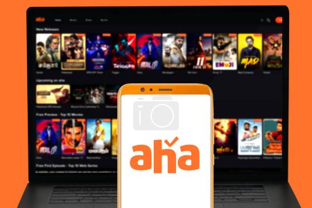 Téléchargez les photos : Logo du service Aha Streaming sur écran mobile et leur site Web flou affiché sur écran d'ordinateur. focus sélectif. - en image libre de droit