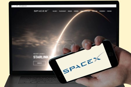 Téléchargez les photos : Logo SpaceX dans l'écran mobile et leur site Web flou affiché dans l'écran d'ordinateur. image éditoriale - en image libre de droit