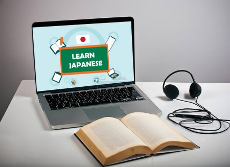 Laptop-Bildschirm zeigte lernen japanischen Poster und ein Buch mit Headset in weißem Tisch. isoliert auf grauem Hintergrund. Selektives Fokusbild.