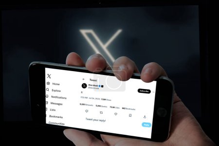 Foto de Página de Twitter Elon Musk en pantalla móvil y logo X en fondo borroso de pantalla para portátil. - Imagen libre de derechos