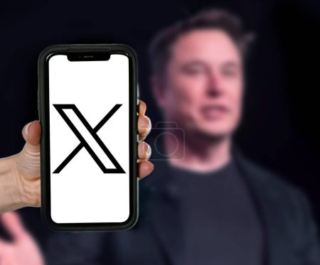 Foto de Logotipo de Twitter X en la pantalla móvil y Elon almizcle imagen borrosa en el fondo del portátil. - Imagen libre de derechos