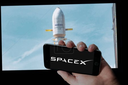 Téléchargez les photos : Logo SpaceX en tenant l'écran mobile et Hughes Jupiter 3 lancement en arrière-plan d'écran d'ordinateur flou. - en image libre de droit