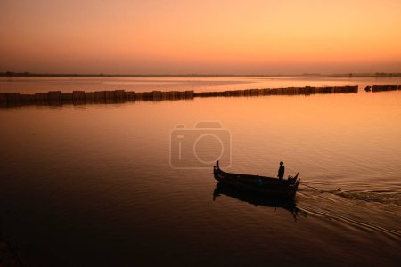 Foto de En Mandalay, la segunda ciudad más grande de Myanmar, un pequeño barco remó tranquilamente a través del río Irrawaddy bajo el atardecer. - Imagen libre de derechos