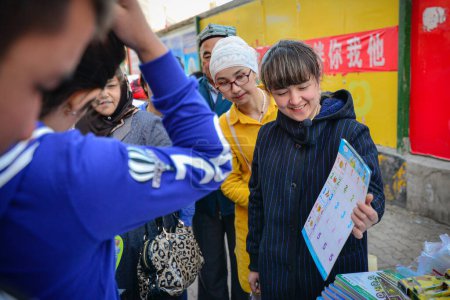 Téléchargez les photos : Vendeurs vendant des cahiers d'exercices pour les enfants et la foule de spectateurs sur le marché traditionnel en plein air à Urumqi, Xinjiang, Chine - en image libre de droit