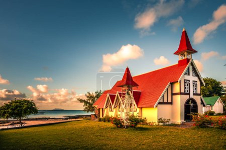 Foto de Puesta de sol en la playa. Iglesia en Mauricio, con un techo rojo y frente al mar. Capa malheureux - Imagen libre de derechos