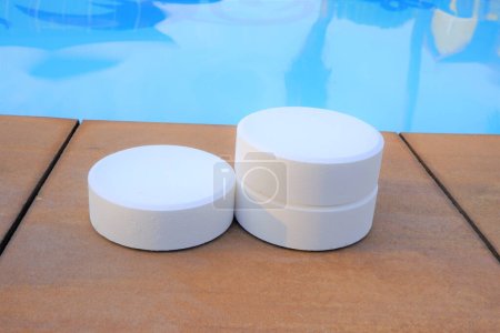 Foto de Chlorine tablets on the edge of swimming pool with blue water background,closeup of chlorine tablets for  pool cleaning. - Imagen libre de derechos