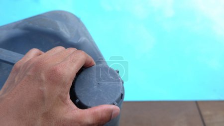 Téléchargez les photos : Main masculine ouvrant le couvercle d'un gallon contenant piscine chemicals.pool contrôle de la qualité de l'eau et l'entretien. - en image libre de droit