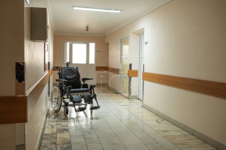 Téléchargez les photos : Lit médical postopératoire et fauteuil roulant sont situés dans le couloir du service hospitalier hospitalisé. Photo de haute qualité - en image libre de droit