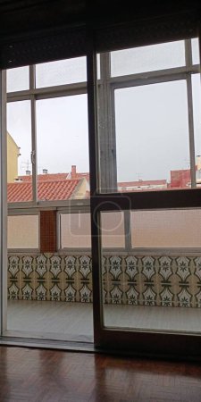 Téléchargez les photos : Une vue de la chambre d'un vieil appartement à Lisbonne à travers le balcon sur les toits et pluvieux - en image libre de droit